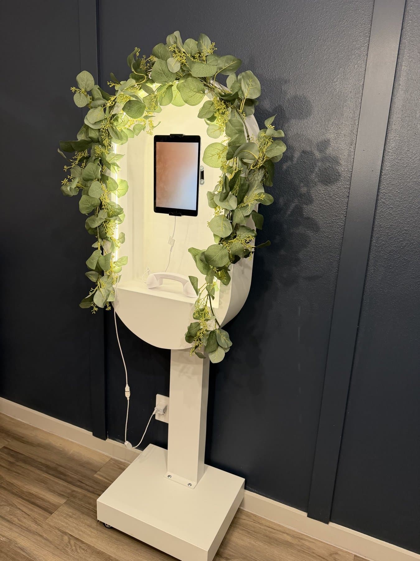 The Video Guestbook kiosk from the side, showing the slim pedestal, wheeled base and eucalyptus-wrapped arch