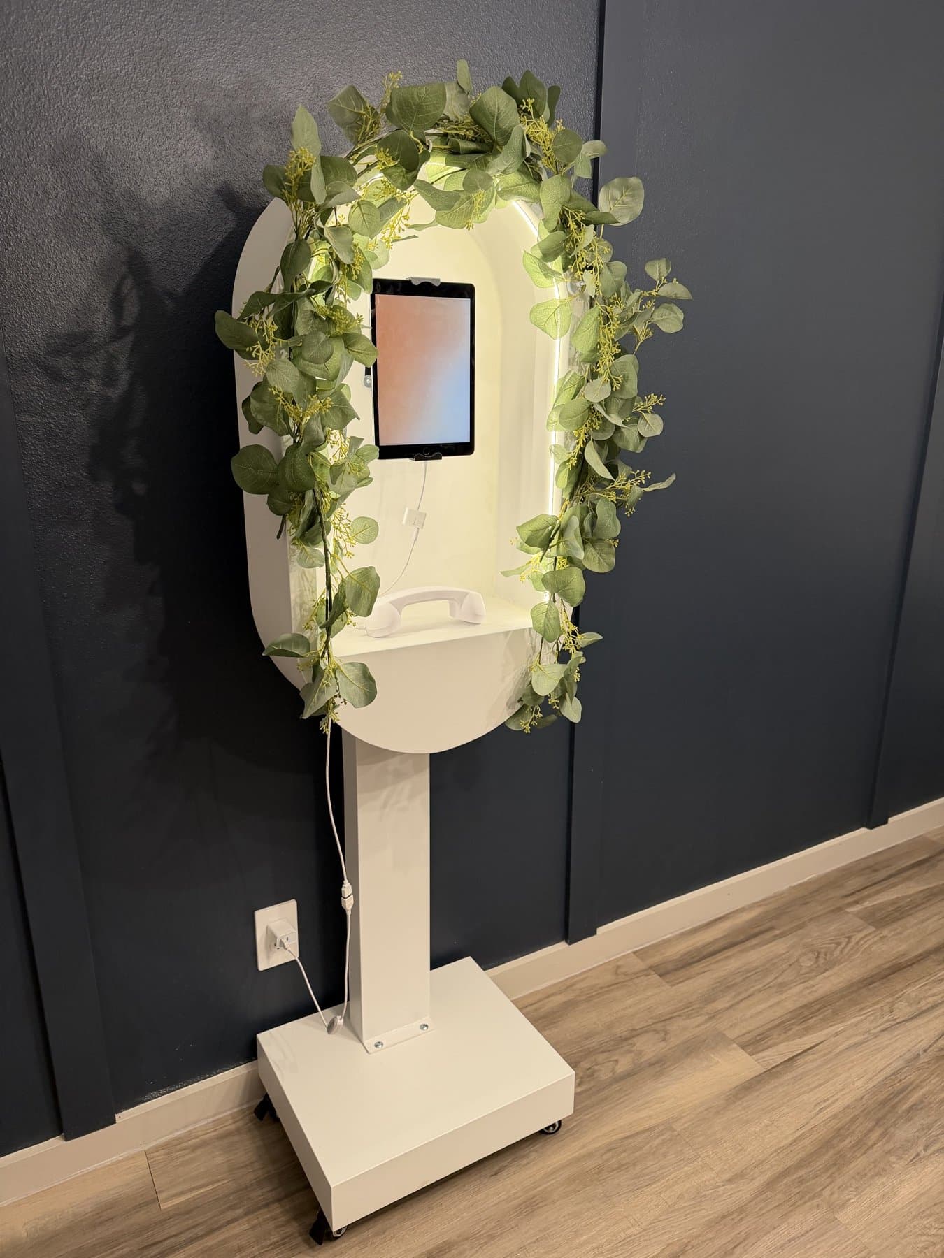 Three-quarter view of the Video Guestbook kiosk with its glowing arch, iPad screen and white handset on the shelf